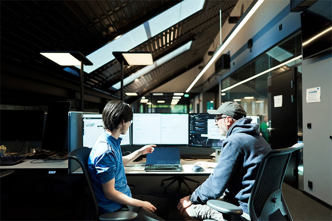 Two men are discussing the information shown on the computer screens.