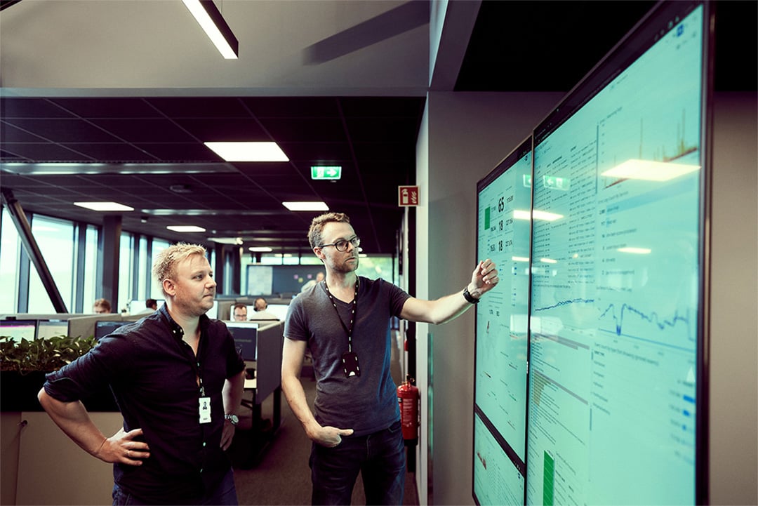 Two men are analyzing data on large wall-mounted screens.